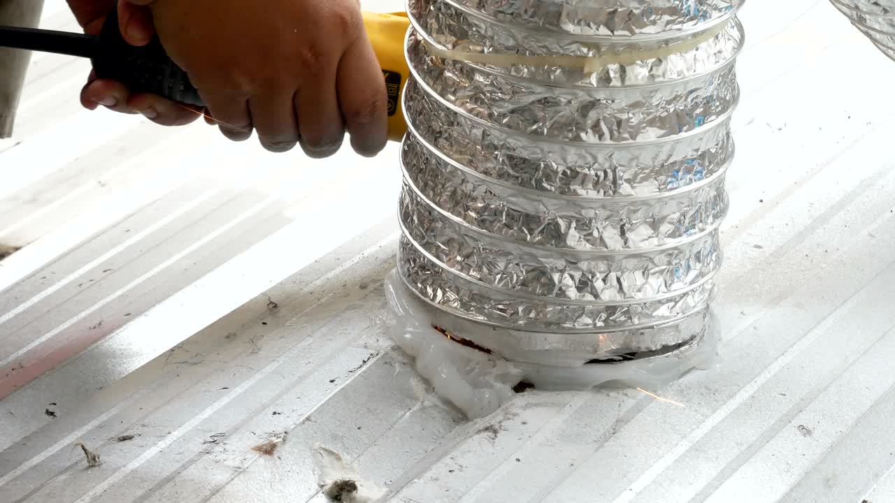 남성의 손은 전기 도구를 사용하여 반이고 연기가 있는 아연 판을 고 잘라내고 있습니다.