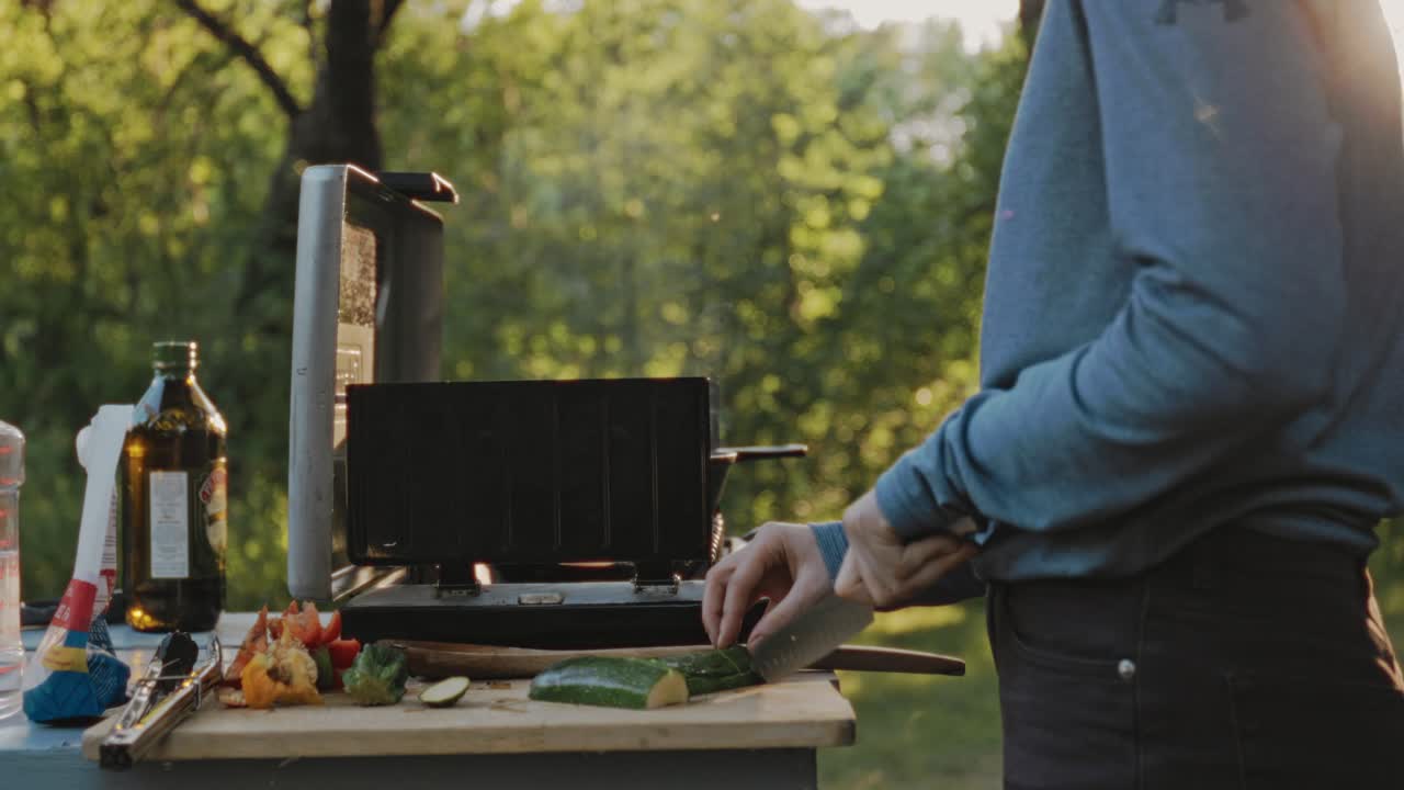 primer plano de un hombre cortando verduras en una tabla de madera, añadiendo a la estufa de gas