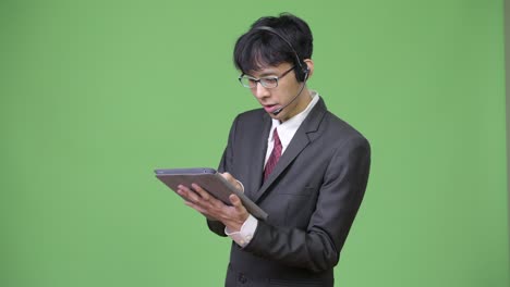 young happy asian businessman using digital tablet while working as call center representative
