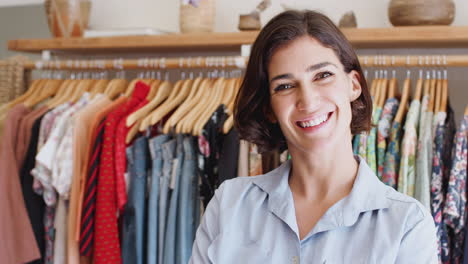 retrato de la propietaria de una tienda de moda de pie frente a la ropa en los rieles