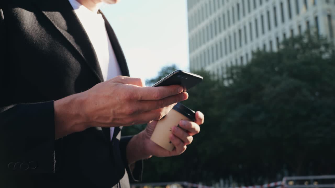 Man businessman boss making call with two phones smartphones, using applecation, walking near his office center in a dark business suit, Experienced CEO entrepreneur in modern office district
