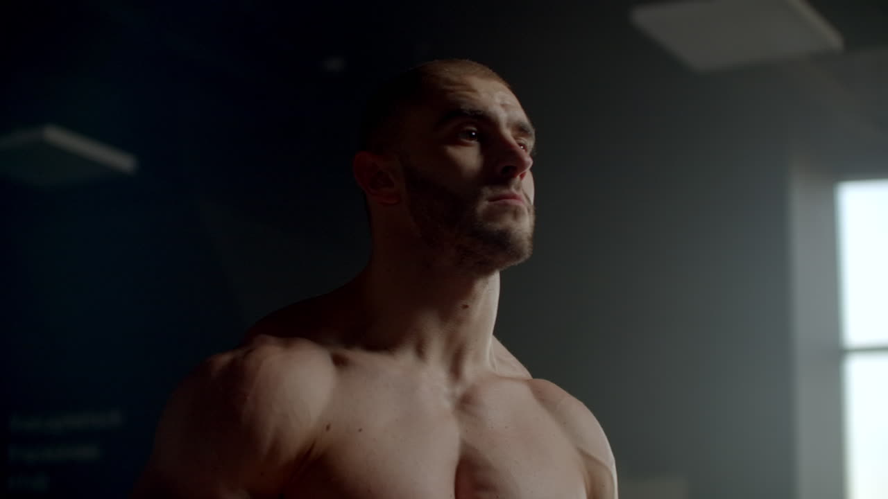 티셔츠를 입지 않은 남자가 기다리고 운동에 적응합니다. 기대. 결정적인 운동 운동 선수를 수행 할 준비가되어 있습니다. 창문 근처에 체육관에 종사하는 강한 남자.