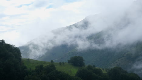 landscape view of a mountain partly covered by clouds the mountain is also partly covered with green vegetation and trees can be seen in the foreground