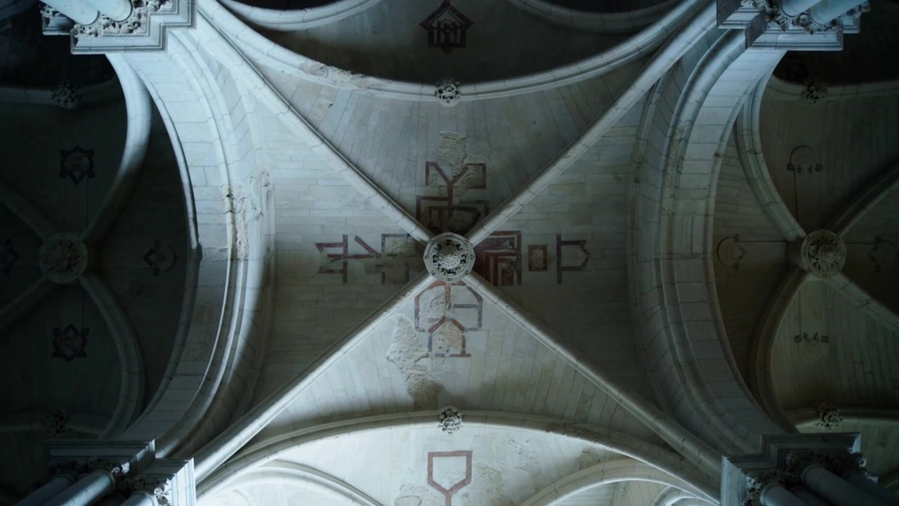 Mostrando la crociera centrale con volta a costoloni all'interno di una chiesa in pietra, luce mutevole che rivela il concio chiave e i motivi.