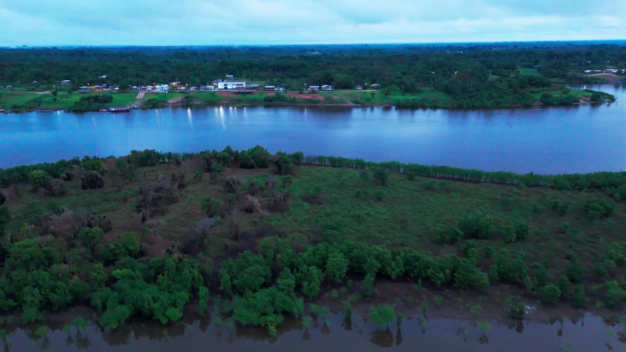 Cinematic aerial view, peaceful riverside village at sunrise along the Amazon River in Brazil, surrounded by tropical rainforest and calm reflective water