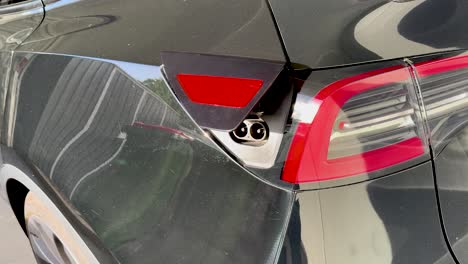 a person inserts an electric vehicle charging cable into a rear port of a black car in bright daylight, with close-up camera movement