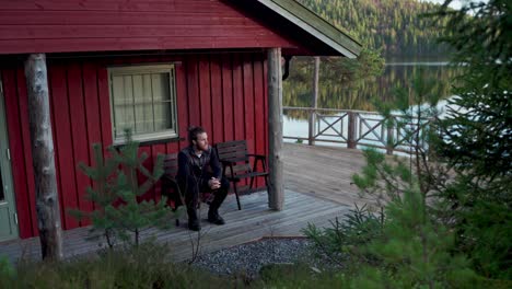 man sitting and looking around at the back of cabin near beautiful lake