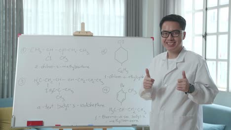 asian male teacher with glasses showing thumbs up gesture and smiling to camera while teaching chemist at home