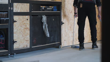 medium shot of young man sweeping workshop, sideways dolly