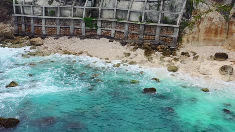 crystal clear turquoise waves crash on rocky beach at blue lagoon on nusa ceningan island, aerial