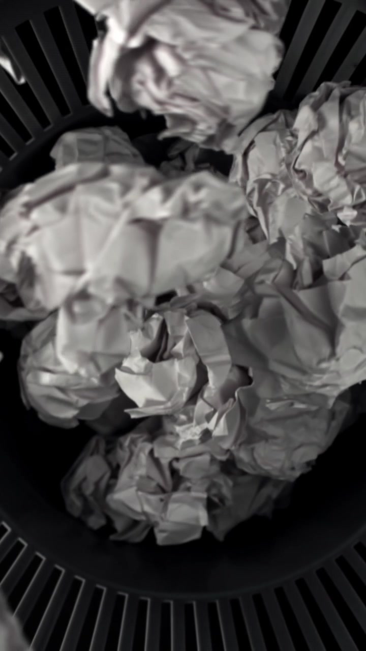 Bolas de papel amassadas caindo em uma lixeira preta