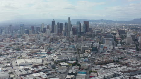 AERIAL:-Slowly-Circling-Downtown-Los-Angeles-Skyline-with-Warehouse-Art-District-in-Foreground-with-Blue-Sky-and-Clouds