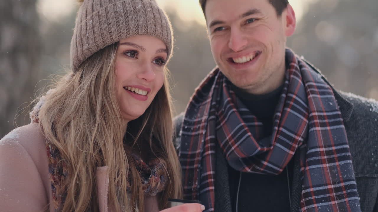 Couple in love in the winter forest to drink tea from a thermos. Stylish man and woman in a coat in the Park in winter for a walk.