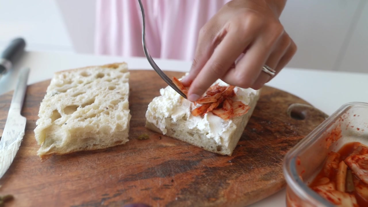 Persona che prepara toast al kimchi con formaggio spalmabile in cucina.