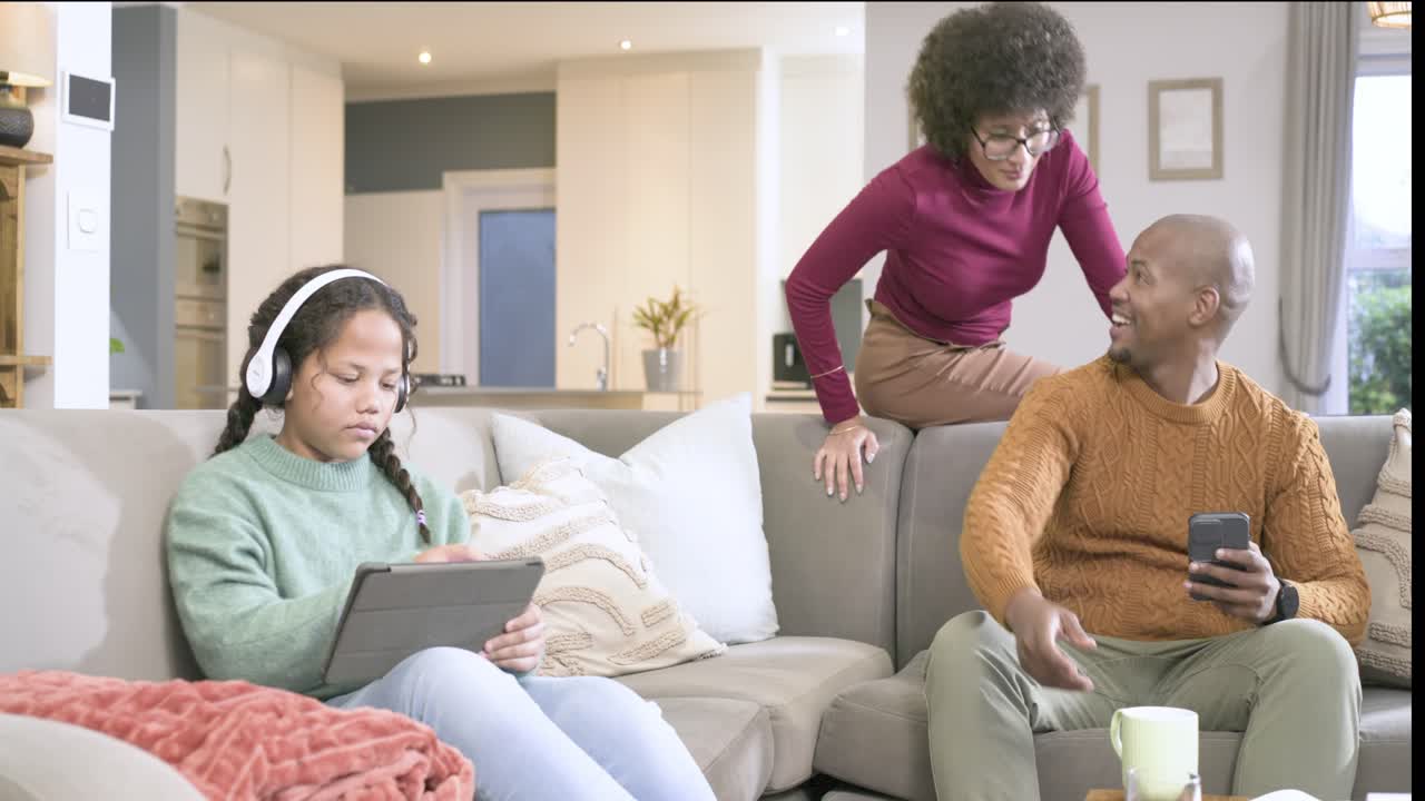African American family connecting on sofa, mother touching dad's shoulder, girl lowering tablet