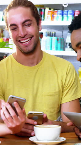 tres amigos usando teléfonos móviles mientras tienen una taza de café
