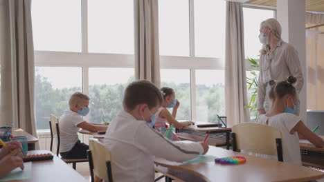 at school in the classroom children write in notebooks in protective masks observing a social distance. school education during the pandemic