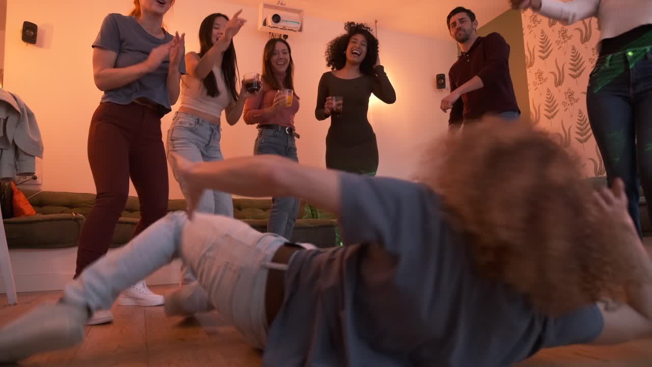 Excited friends cheering for man performing stunt on floor during weekend party at home