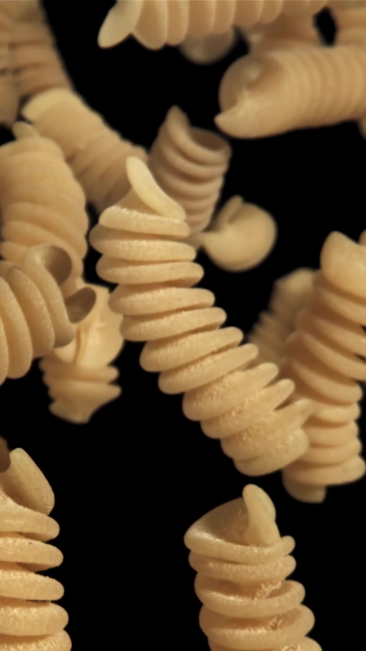Pasta fusilli cruda che cade al rallentatore su sfondo nero