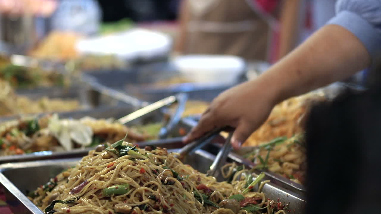 primer plano de la persona que prepara fideos fritos tradicionales en el mercado de comida callejera durante la noche en bangkok