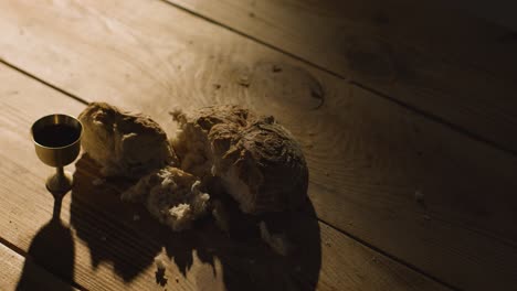 concepto religioso filmado con cáliz pan roto y vino en una mesa de madera con un charco de luz