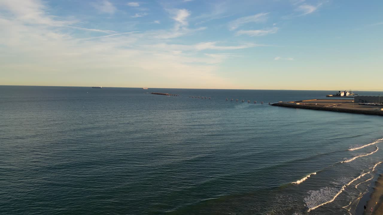 flight on a beach watching people stroll and a close up of an old unused pier in the sea with several boats in the background with a blue sky with clouds on a winter day in Valencia Spain