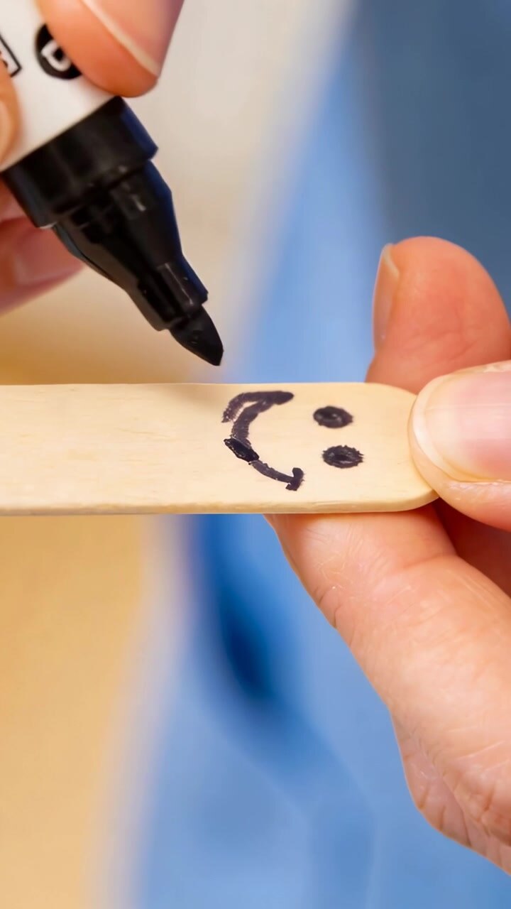 Vertical video: Drawing hands touching tip to stick at desk, rotating to finish smile with marker