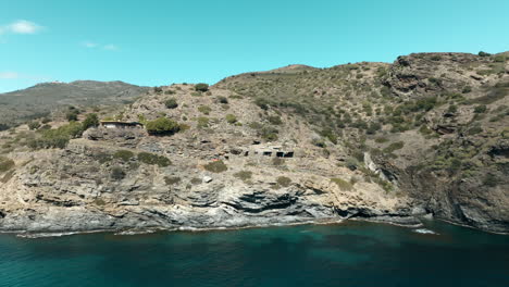 Vuelo-Aéreo-Hacia-Atrás-Desde-Una-Gran-Casa-Construida-Sobre-Acantilados-Costeros,-Cap-De-Creus,-España