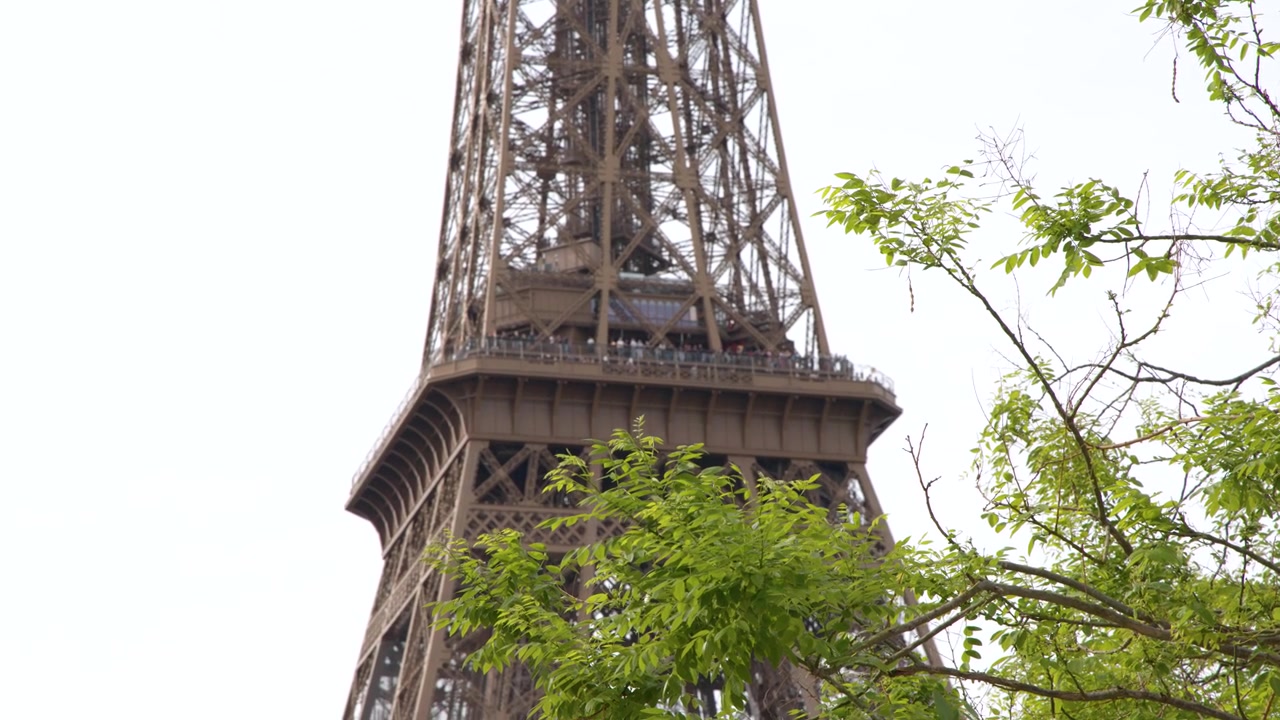 Inquadratura media statica del monumento a traliccio di ferro dietro rami di alberi verdi sotto un cielo coperto