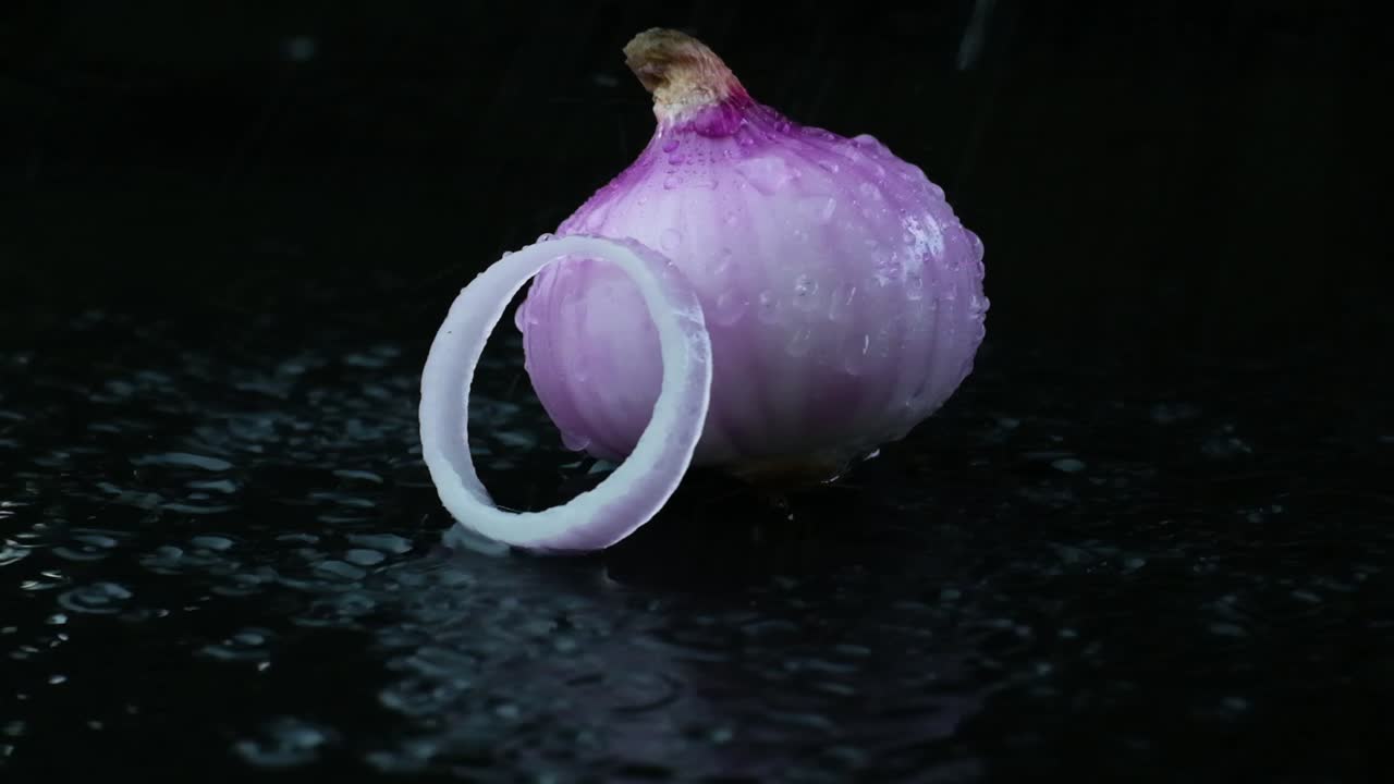 Water droplets falling on bulb of red onion in pool of water