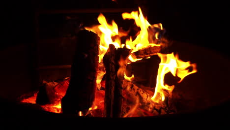 Campfire-flames-burn-firewood-slowly-during-night-at-outdoor-campsite