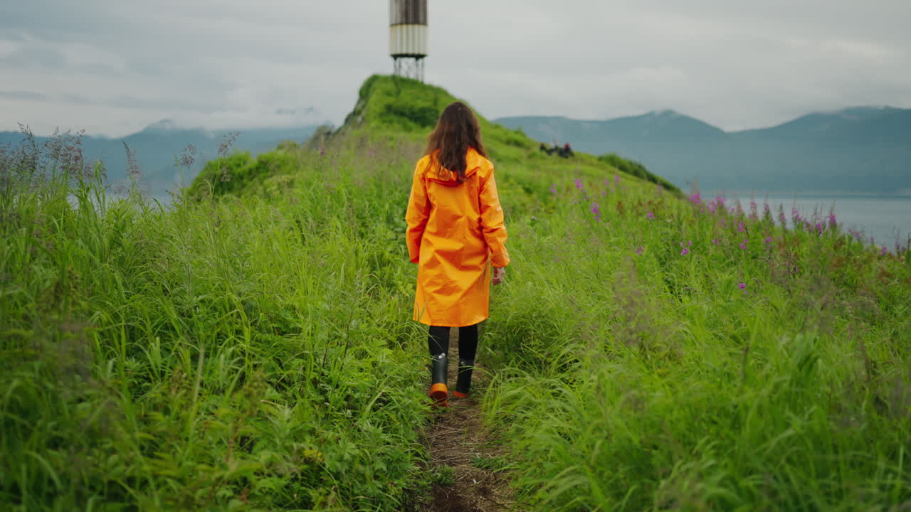 Woman in Orange Raincoat Hiking on a Coastal Path