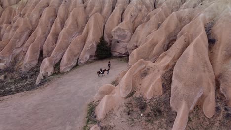 aerial shot of tourists riding horses next to fairy chimneys in cappadocia, turkey