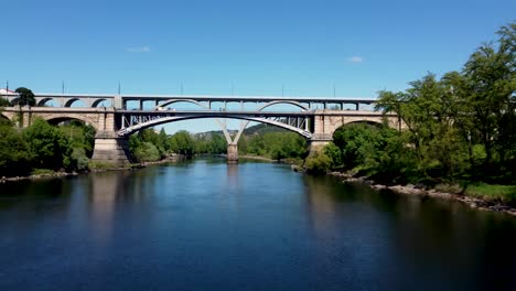 fly low over river towards ancient arch bridge with traffic, ourense