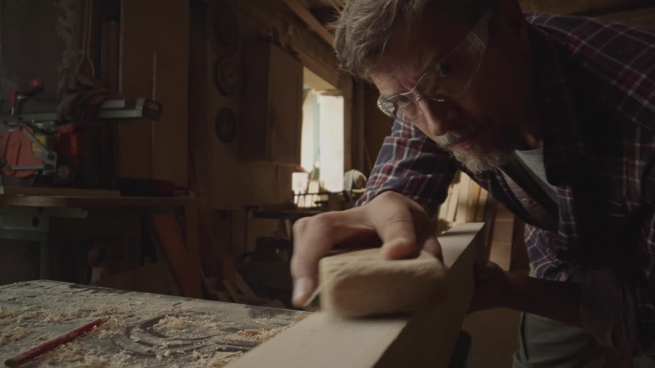 A carpenter is sanding a piece of wood in a workshop
