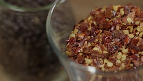 Closeup-of-glass-jars-with-spices,-crushed-red-pepper-and-whole-black-pepper-in-the-background