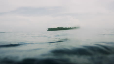 Small-atoll-tropical-island-off-in-distance-behind-calm-ocean-water-surface