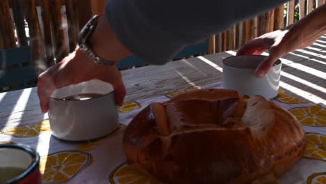 a-cook-places-two-hot-cups-of-tea-on-a-table-with-a-brioche,-outdoor-dining,-wooden-table