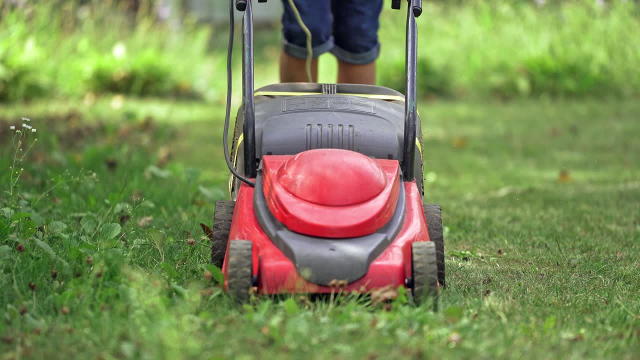 Young boy cutting the grass with a lawn mower in summer time