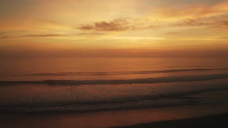 cinematic aerial shot moving towards the sea over sand dunes and long grass, as the sun fades into clouds over the horizon