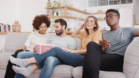 Grupo-De-Amigos-Sentados-En-El-Sofá-Y-Viendo-Películas-En-Casa-Mientras-Comen-Palomitas-De-Maíz