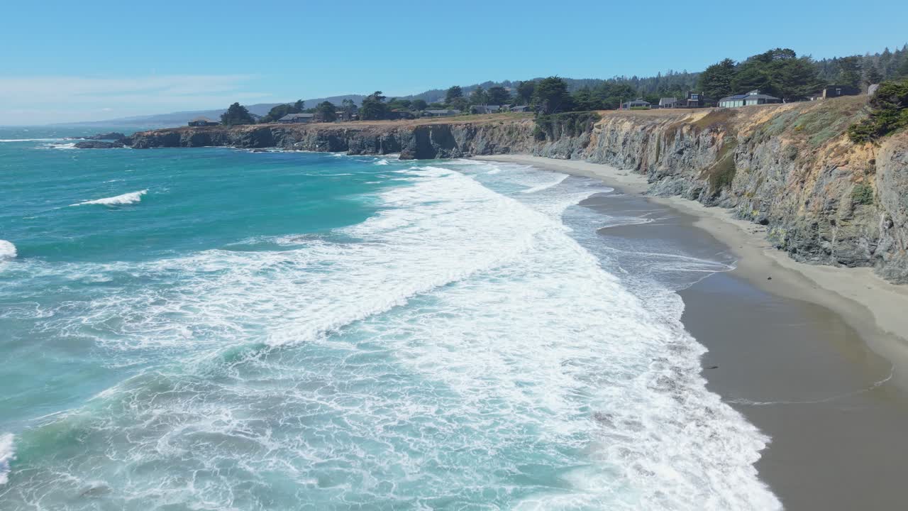 The drone moves backward from the shore, revealing crashing waves and white foam spreading across Black Point Beach, California