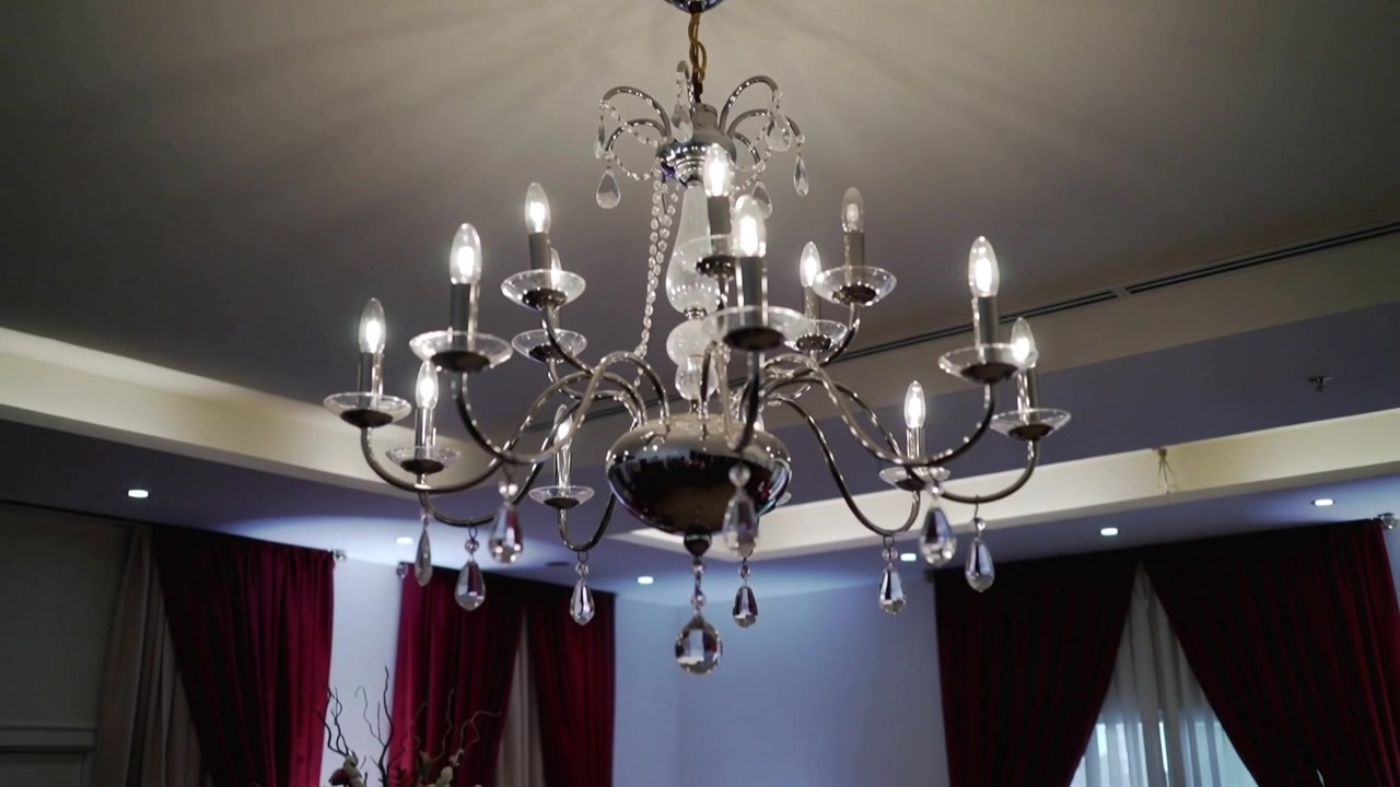 Telecamera che si allontana rivelando un grande lampadario a più bracci sopra una sala da pranzo formale, mostrando una tavola apparecchiata.