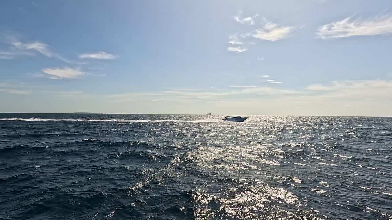 A speedboat glides across the sparkling ocean under bright sunlight in Phuket, Thailand, creating a serene and dynamic scene