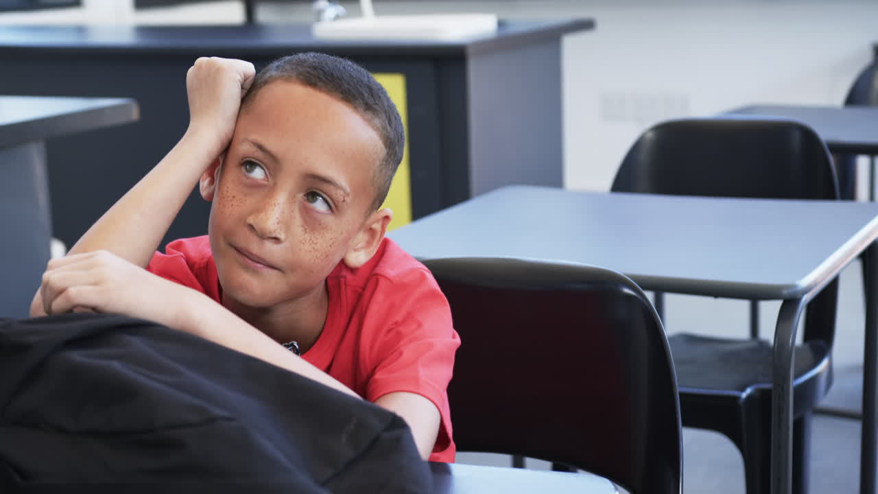un niño biracial con pecas se sienta pensativo en un aula de la escuela