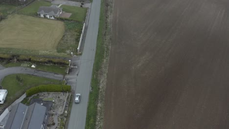 Aerial-tracks-vehicle-driving-on-narrow-country-road-in-rural-Ireland