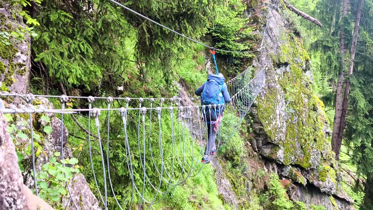 Hikers on precarious bridge, Ferrata Hans Kammerlander trail in the Alta Badia Dolomites, Italy, slow-motion showcasing rocky landscapes and alpine beauty
