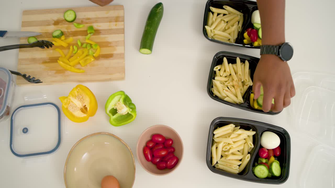 Video vertical: Manos preparando comidas, cortando pepino y colocando pasta, verduras y pollo en recipientes.