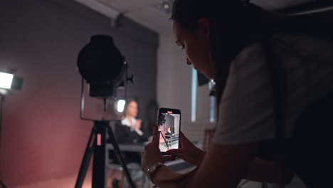 long-haired girl in white shirt takes a video on smartphone. blogger sits at desk talking for her blog.