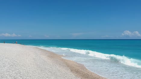 Drone-flying-low-over-a-white-pebble-beach-toward-the-blue-Caribbean-Sea-and-waves-crashing-on-the-shore